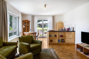 A living room with a sofa, a TV, and a kitchen area with a cabinet and a table.
