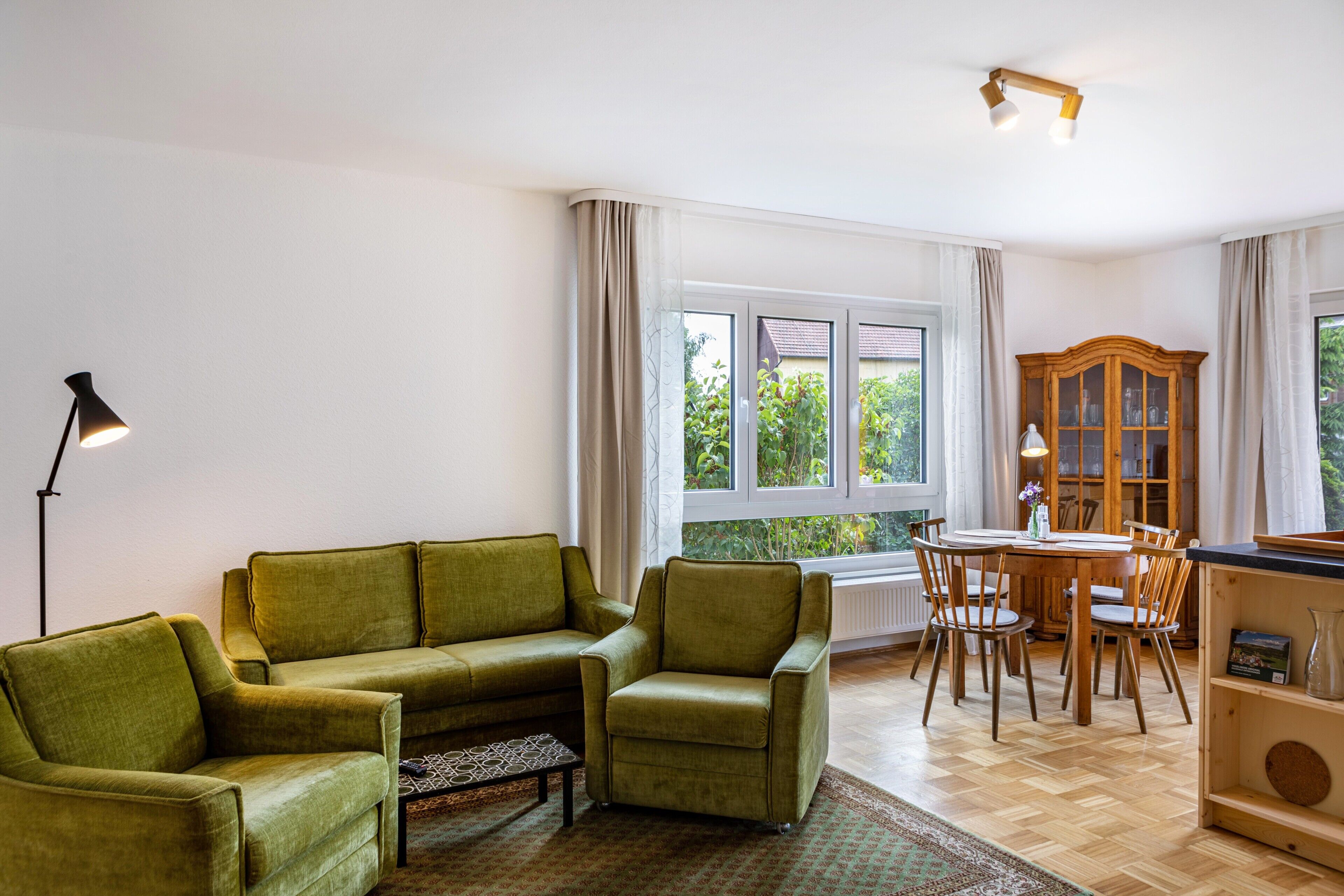 Ein Wohnzimmer mit einem grünen Sofa, einem Esstisch mit Stühlen, einer Lampe und einem Schrank.