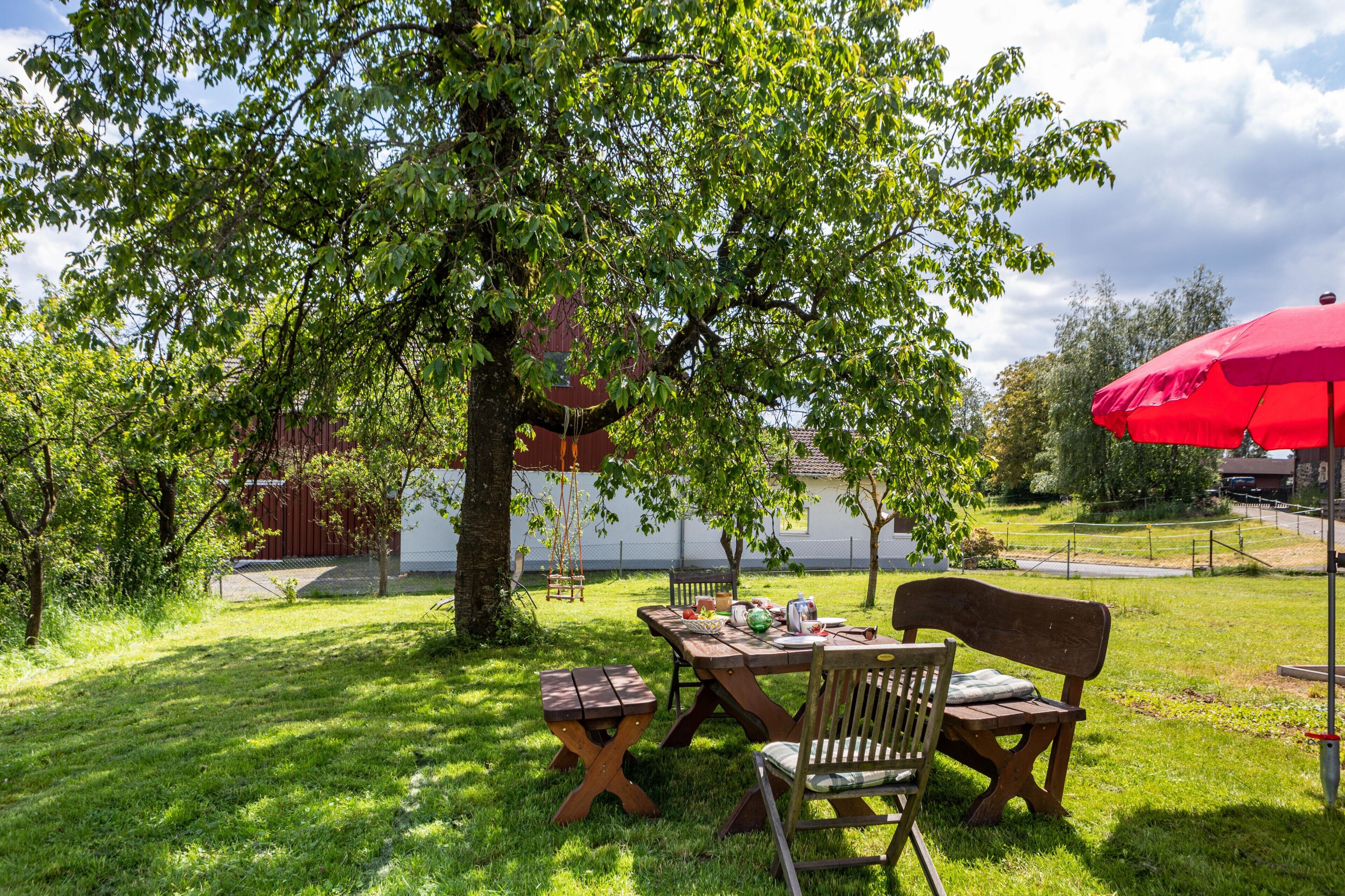 Een terras met een houten tafel, stoelen en een rode parasol.