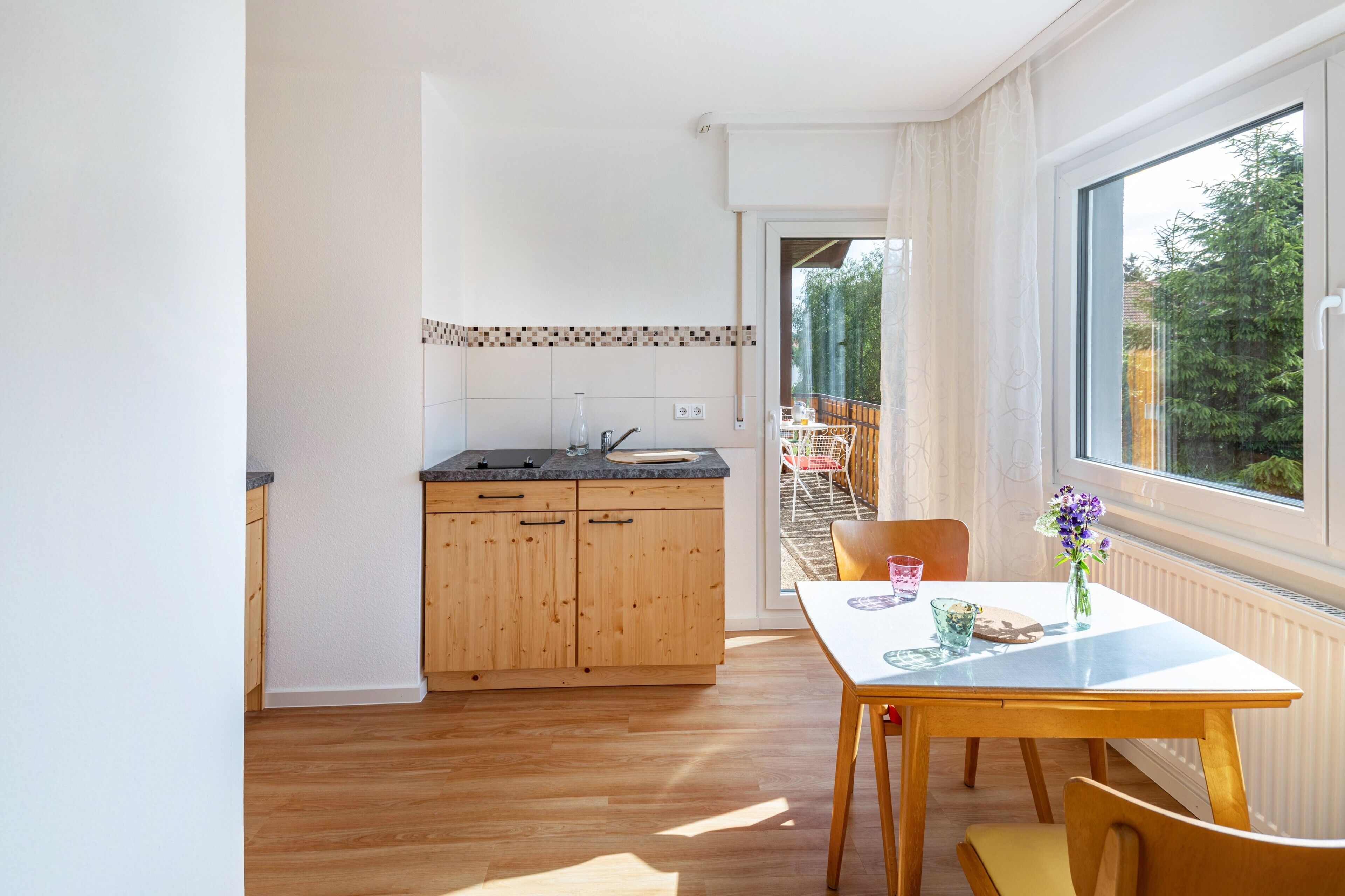 Una cocina con armarios de madera, una mesa de comedor con sillas y vistas a un área exterior por una puerta abierta.