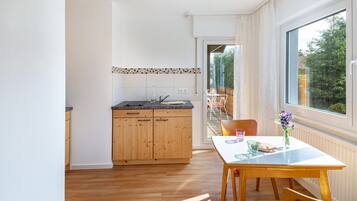 Una cocina con armarios de madera, una mesa de comedor con sillas y vistas a un área exterior por una puerta abierta.