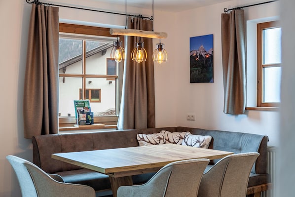 A cozy dining area with a wooden table, cushioned seating, and pendant lighting.
