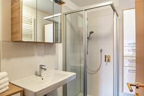 Un baño con ducha de vidrio, lavamanos blanco y espejo sobre el lavamanos.