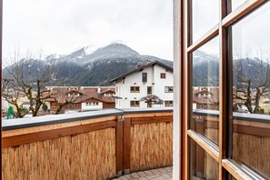 A balcony with a wooden fence, a view of a mountain, and a building with multiple windows.