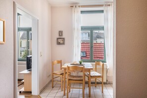A dining area with a table, chairs, and a view of buildings through a window. - Apartment 'Abendsonne' with Wi-Fi (Ostseebad Kühlungsborn)