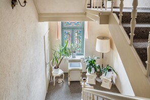 A staircase with a white railing, a window with stained glass, and potted plants on a small table. - Apartment 'Abendsonne' with Wi-Fi (Ostseebad Kühlungsborn)