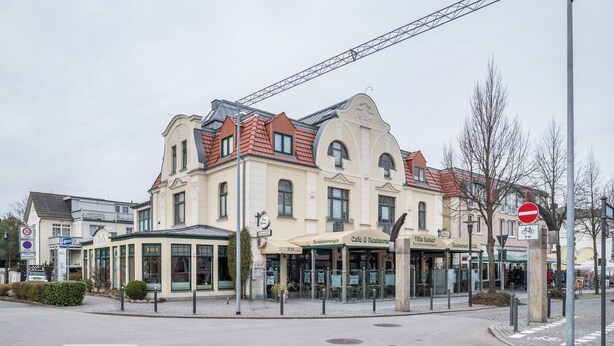 Ein mehrstöckiges Gebäude mit einem Café und Restaurant im Erdgeschoss, einer überdachten Außenbereich-Sitzgelegenheit und einem Verbotsschild.