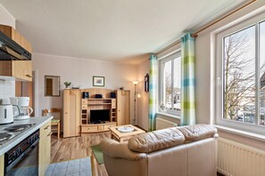 Un espace de vie compact comprenant un coin cuisine, un canapé, un téléviseur et une fenêtre avec des rideaux.