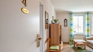 A room with a door marked '4', a wooden chair, a small table, a mirror, and a window with curtains. - Apartment 'Morgensonne' with Wi-Fi (Ostseebad Kühlungsborn)