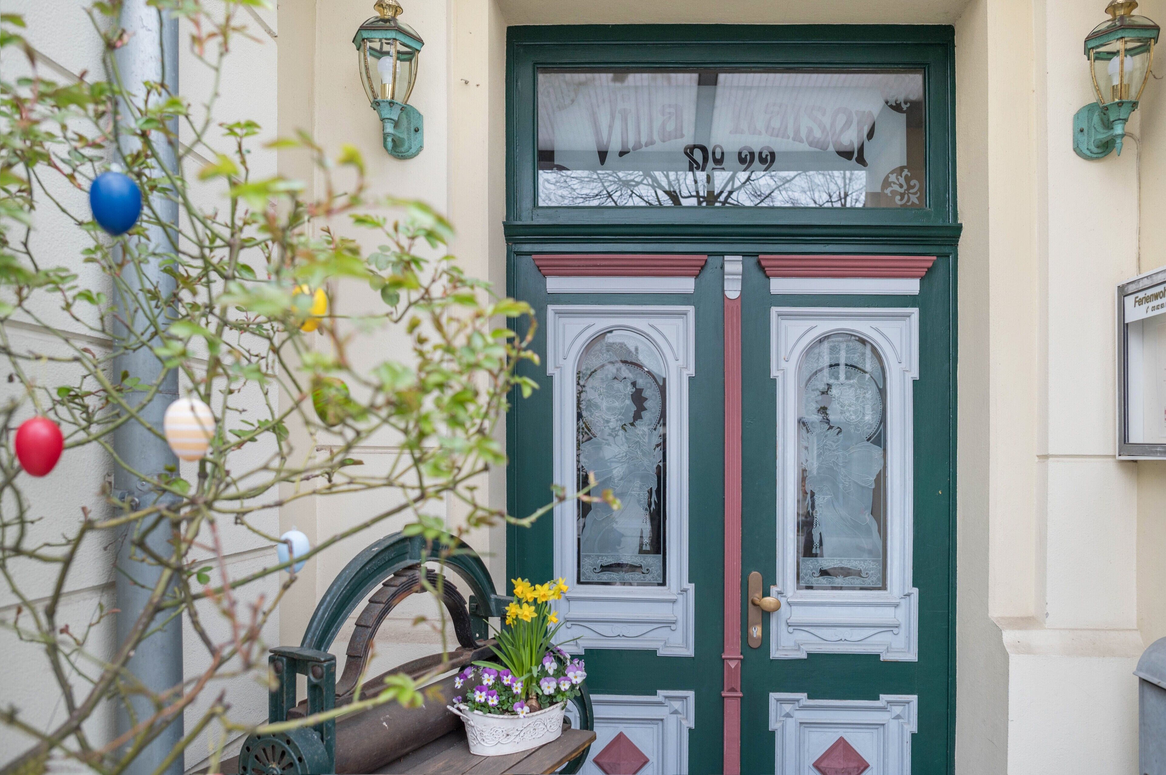 En grön dubbeldörr med ett fönster ovanför, ett litet bord med blommor och en cykel parkerad utanför.