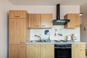 Une cuisine compacte dotée de meubles en bois, d’un évier en acier inoxydable, d’une hotte noire et d’une machine à café.