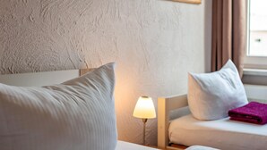 A hotel room with a textured wall, a bedside lamp, two pillows, and a folded towel. - Apartment 'Morgensonne' with Wi-Fi (Ostseebad Kühlungsborn)