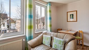 A cozy room with a sofa, a dining table, and a window with curtains. - Apartment 'Morgensonne' with Wi-Fi (Ostseebad Kühlungsborn)