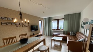 A living room with a wooden dining table, a sofa, a TV, and a chandelier. - Apartment 'Fewo Am Edersee' with Private Garden, Balcony and Wi-Fi (Edertal)