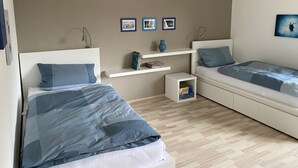 A bedroom with two beds, a nightstand, a shelf with books and a vase, and framed pictures on the wall. - Apartment 'Fewo Am Edersee' with Private Garden, Balcony and Wi-Fi (Edertal)