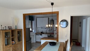 A dining area with a wooden table and benches, a kitchen in the background, and a wall clock. - Apartment 'Fewo Am Edersee' with Private Garden, Balcony and Wi-Fi (Edertal)