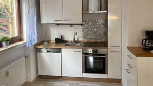 A compact kitchen with white cabinets, a dishwasher, an oven, and a window with curtains. - Apartment 'Fewo Am Edersee' with Private Garden, Balcony and Wi-Fi (Edertal)