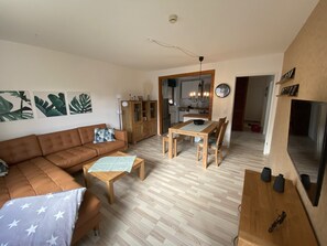 Un salon comprenant un canapé, une table à manger avec des chaises, un meuble en bois et un téléviseur fixé au mur.