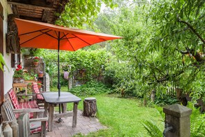 Une terrasse extérieure avec une table et des chaises, entourée d’une végétation luxuriante et d’un pilier en pierre.