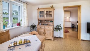 A bedroom with a bed, bedside table, lamp, window with curtains, and a view of the garden.