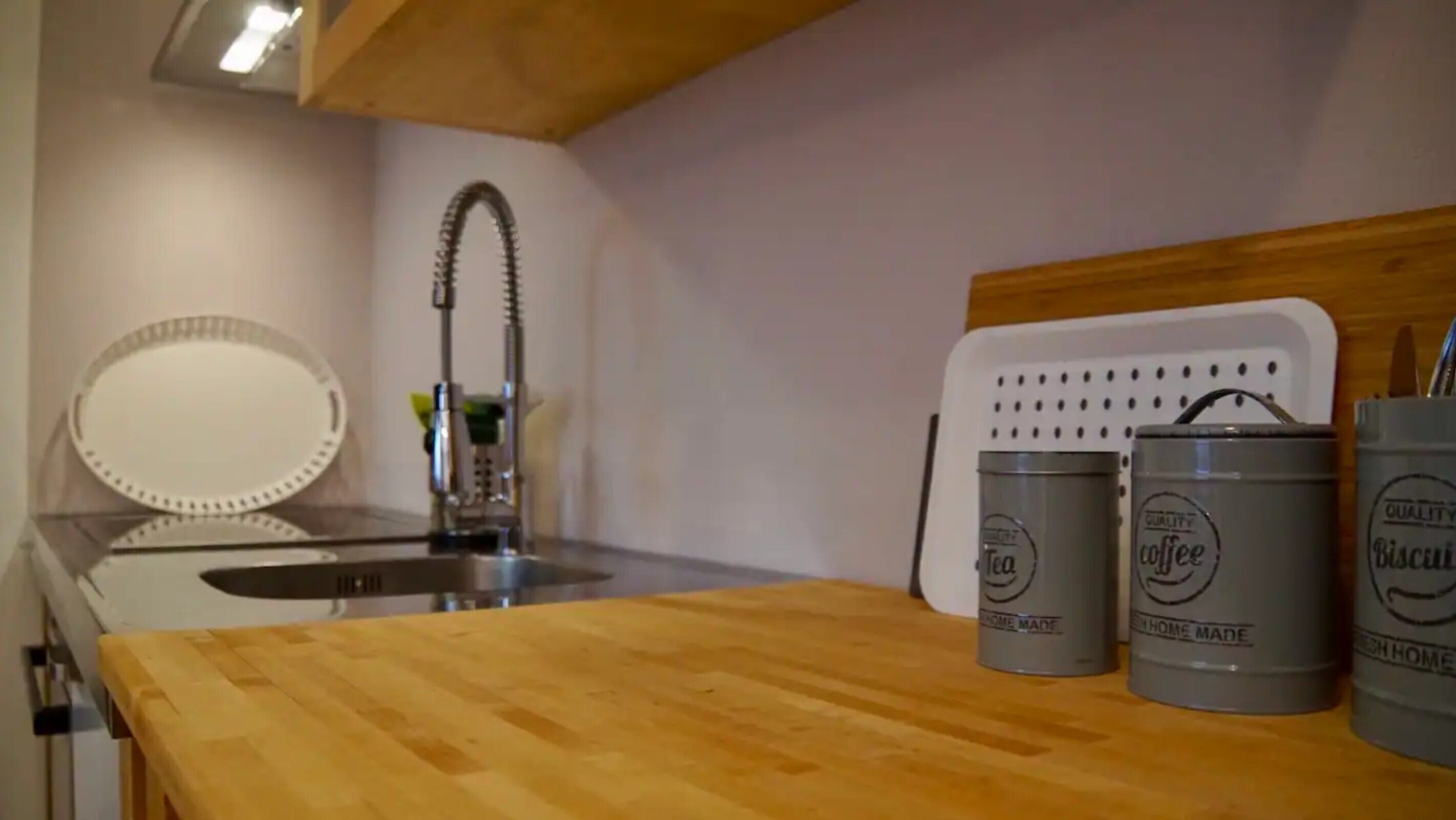 A kitchen with a wooden countertop, a sink, and three grey canisters labeled 'Tea,' 'Coffee,' and 'Biscuits.'