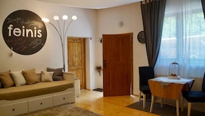 A cozy living room with a sofa, a dining table with chairs, a wooden door, and a wall-mounted light fixture. - Chalet 'Feinis' with Private Terrace, Garden, and Wi-Fi (Waasen)