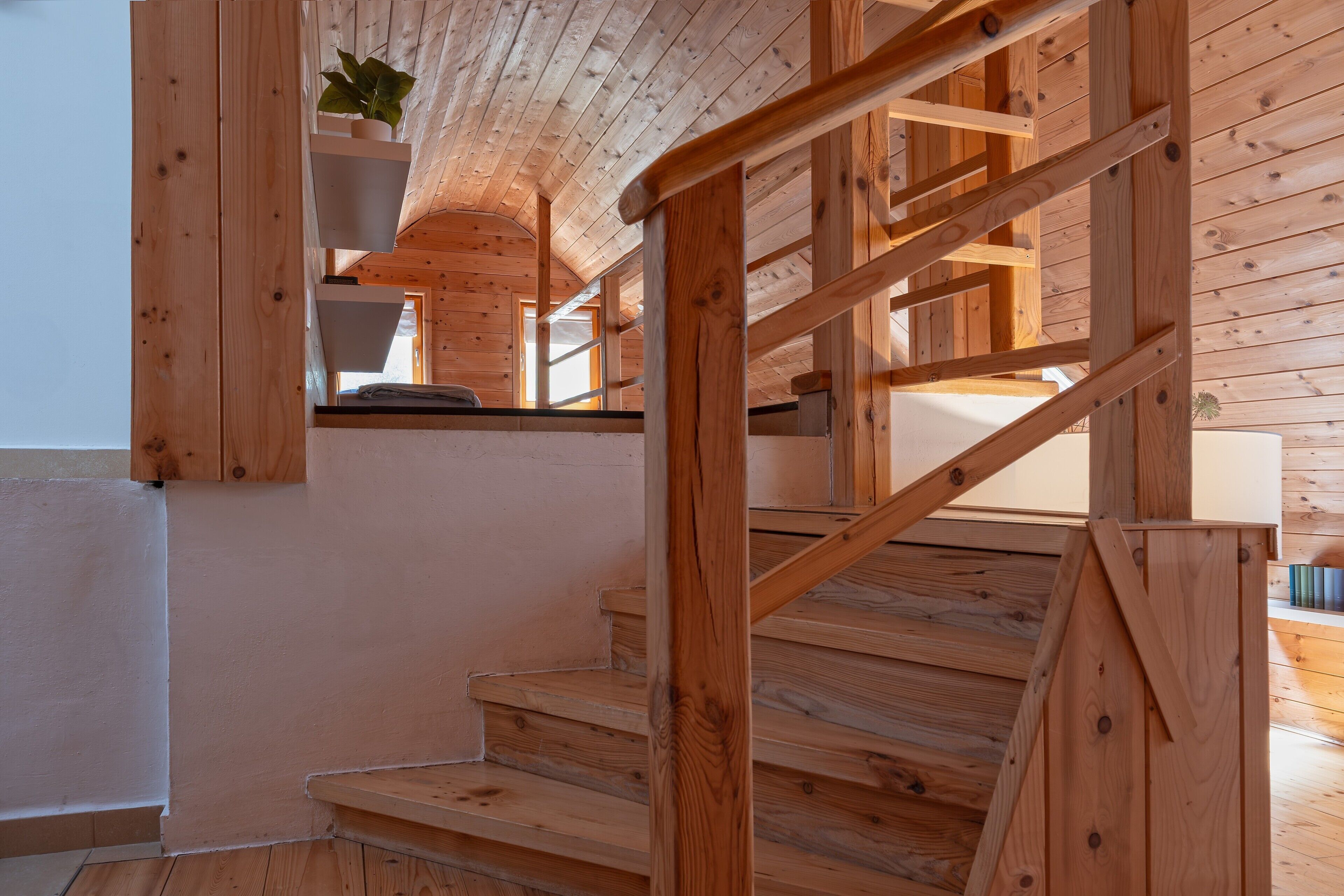 A wooden staircase with a handrail, a potted plant, and a window.