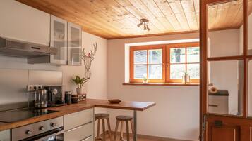 A modern kitchen with wooden ceiling, stainless steel appliances, a window with blinds, and a door with glass panels.