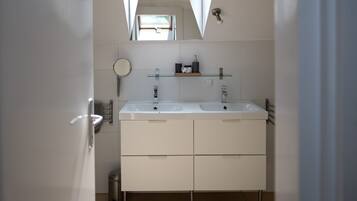 A modern bathroom with a skylight, two sinks, a mirror, and a glass shelf with toiletries.