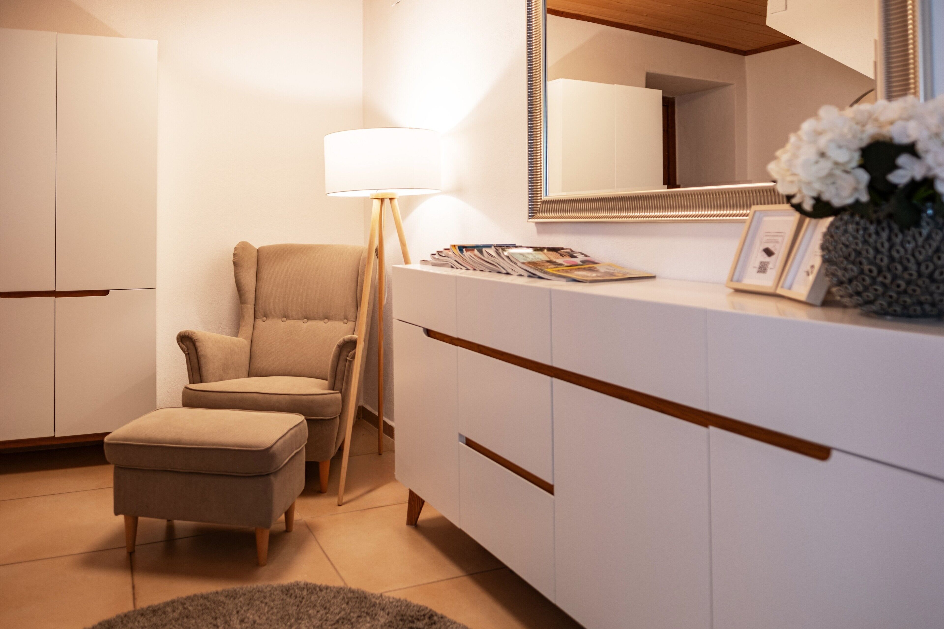Un dormitorio moderno con una cama grande, una mesita de noche con lámpara, una silla y un aparador.