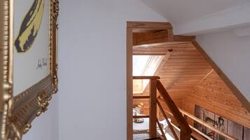 A wooden staircase leading to an upper floor with a skylight, a framed picture on the wall, and a table with a vase of flowers.
