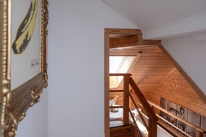 A wooden staircase leading to an upper floor with a skylight, a framed picture on the wall, and a table with a vase of flowers.