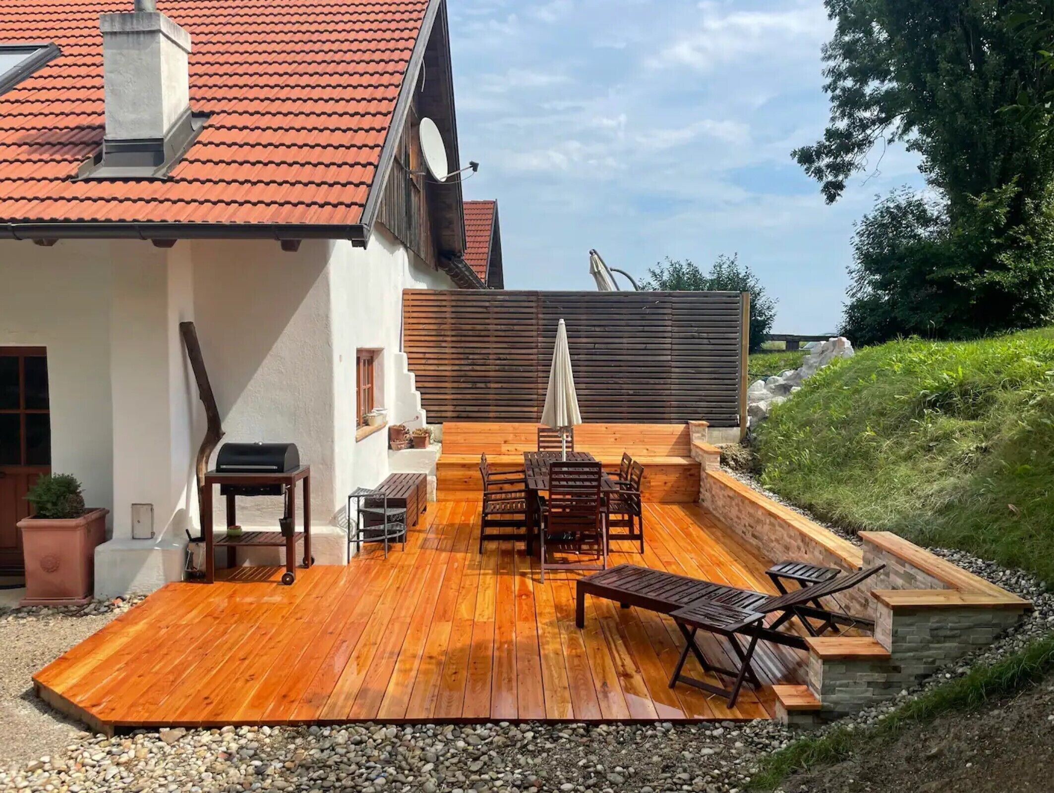 Une terrasse avec une plateforme en bois, du mobilier d’extérieur et un barbecue.