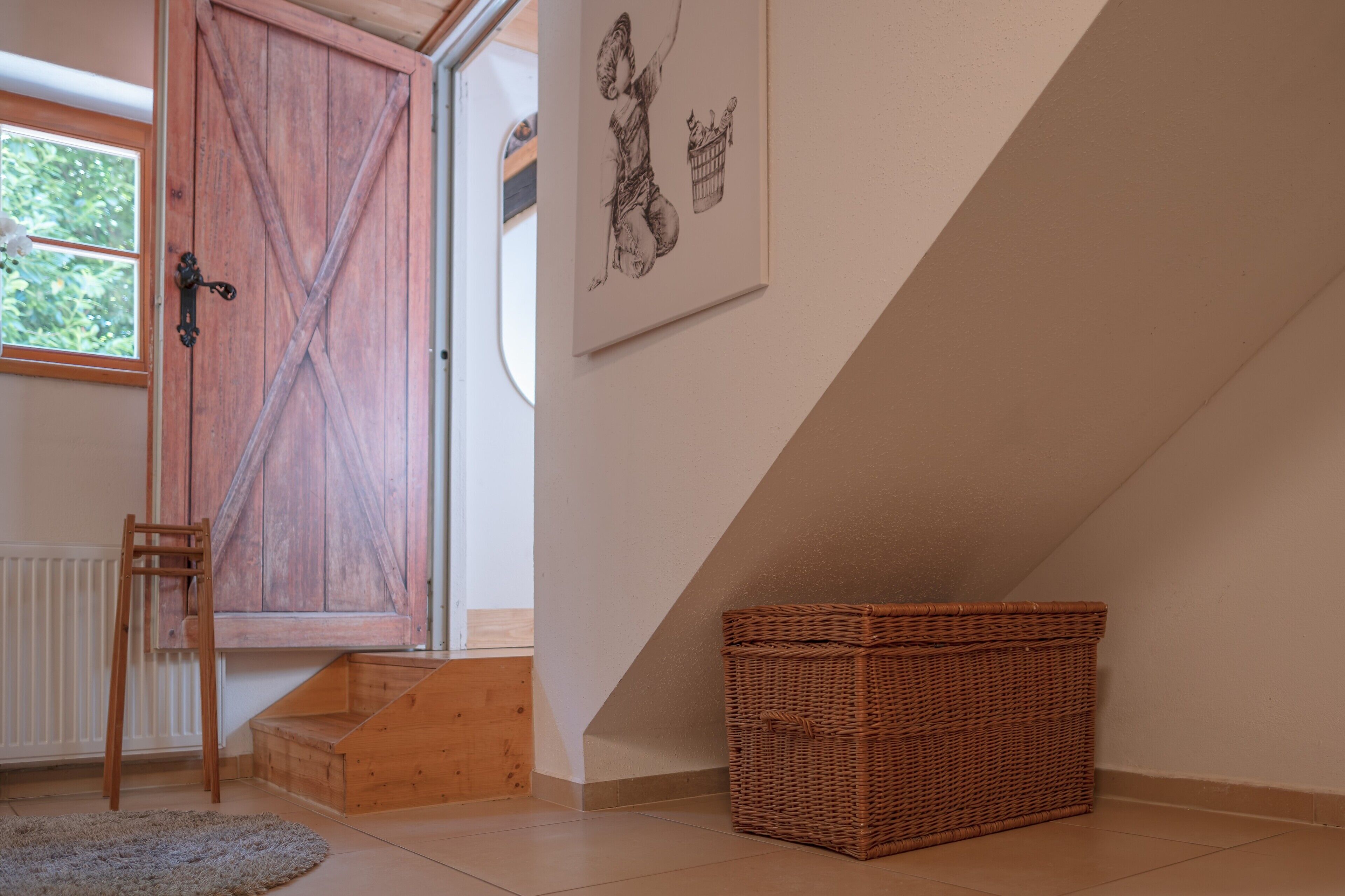 Una habitación con una puerta de madera, una cesta de mimbre y una obra enmarcada en la pared.