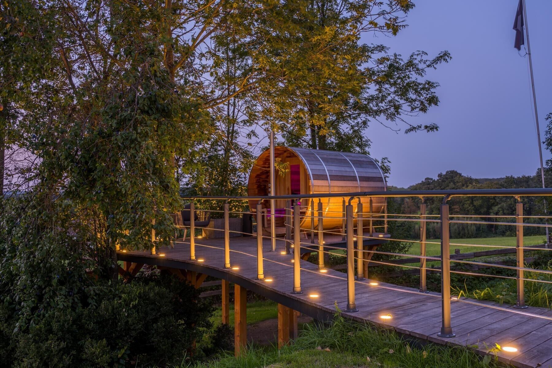 A wooden bridge leading to a cylindrical structure with a red interior, surrounded by greenery.