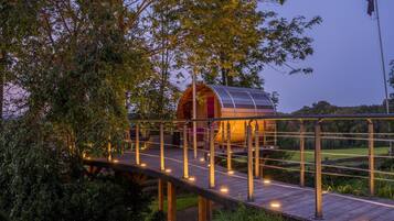 A wooden bridge leading to a cylindrical structure with a red interior, surrounded by greenery.