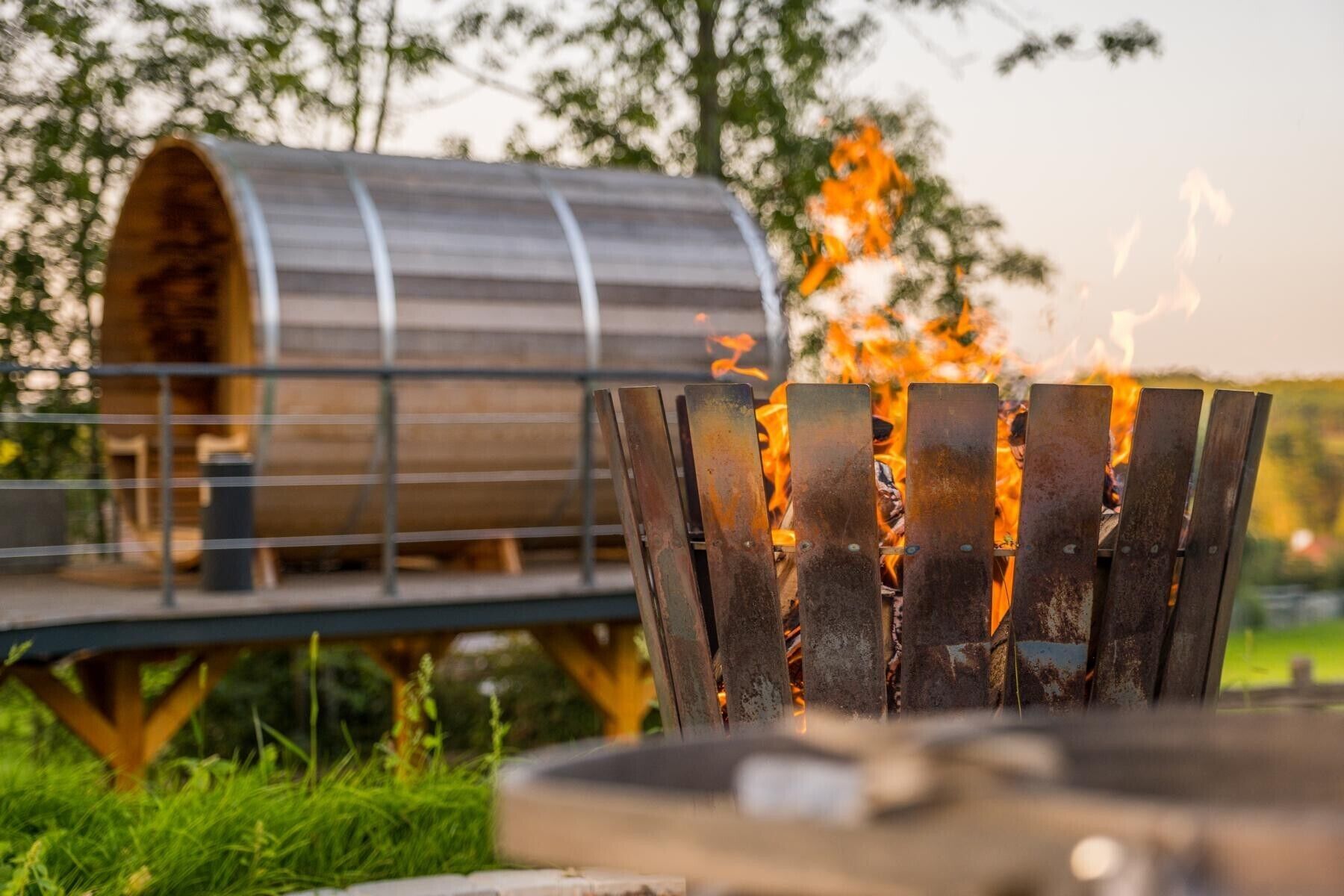 A metal fire pit with flames, surrounded by greenery.