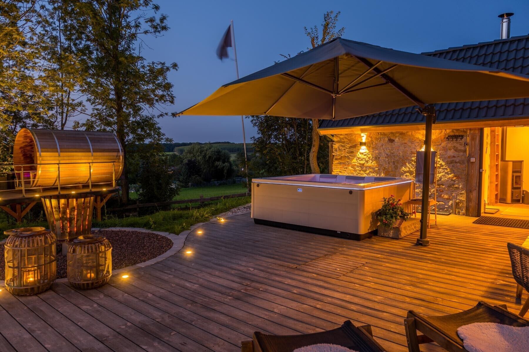 A wooden deck with a hot tub, outdoor seating, and a stone wall.