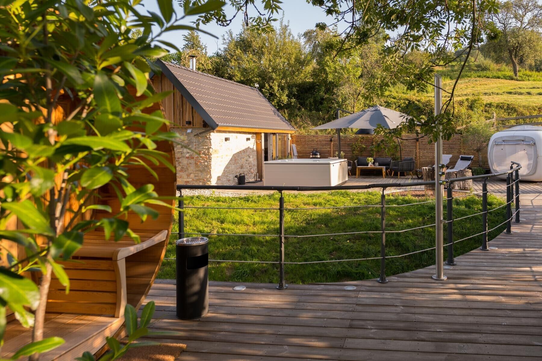 Een houten terras met een jacuzzi, een barbecuegedeelte en een omheinde tuin.