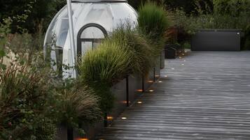 Una terrassa de fusta amb un bany d'hidromassatge, un hivernacle i una filera de plantes.