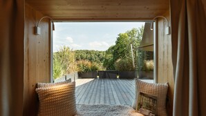 Een houten interieur met uitzicht op een houten terras en begroeiing.