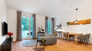 Una sala de estar moderna con un sofá, una mesa de comedor y sillas, un televisor y un ventanal con cortinas.
