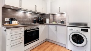 Una cocina moderna con armarios blancos, horno empotrado, cafetera y lavadora.