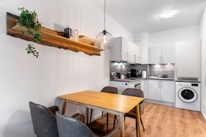 Eine kleine Küche mit Holztisch, Stühlen, einer Pendelleuchte und einer eingebauten Waschmaschine.