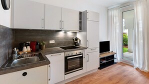 A modern kitchen with a built-in oven, a sink, and a television on a wooden stand. - Studio Apartment 'Km Style  Nr 1' with Private Terrace and Wi-Fi (Freiburg im Breisgau)