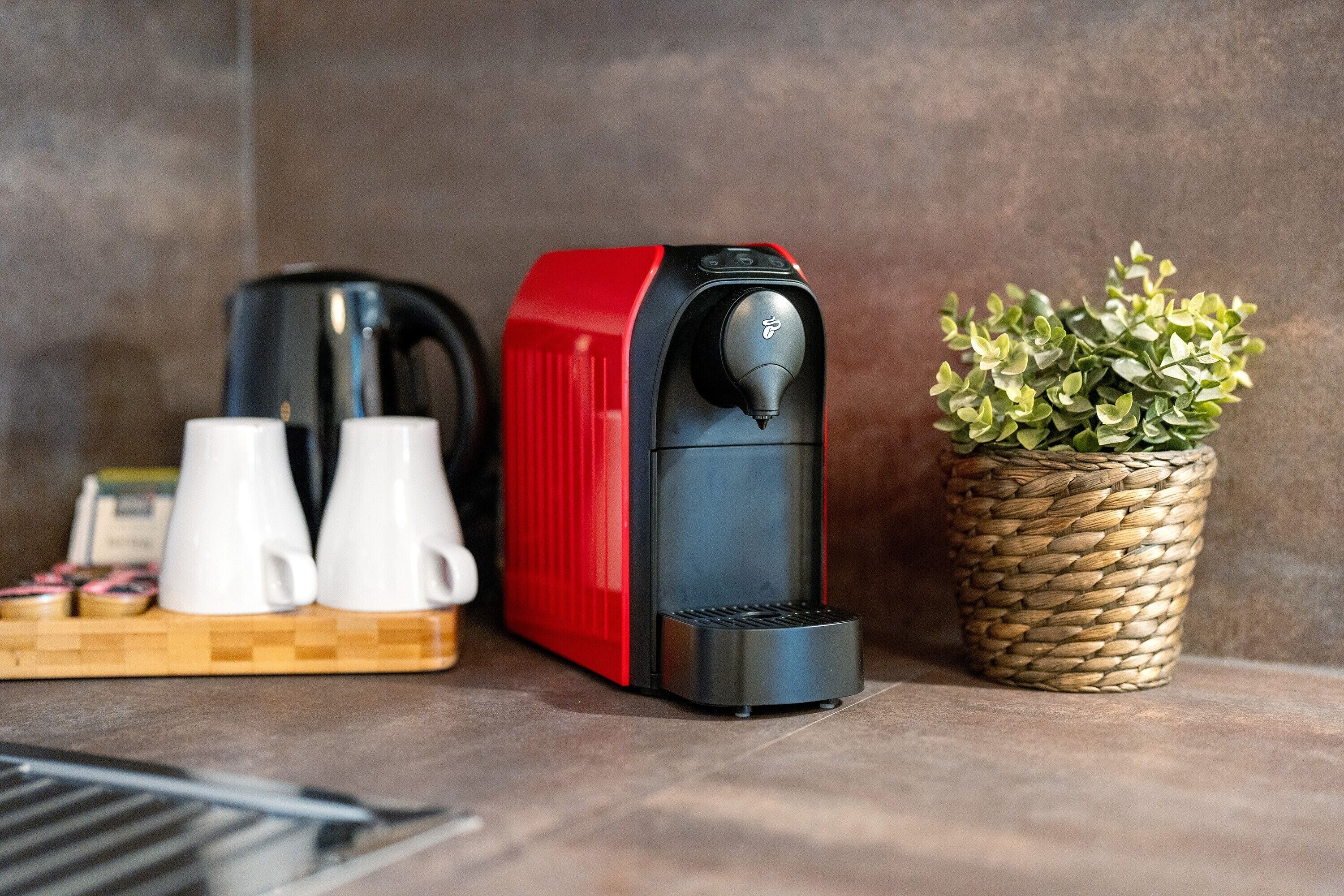 A coffee machine, two white cups, and a potted plant on a countertop.