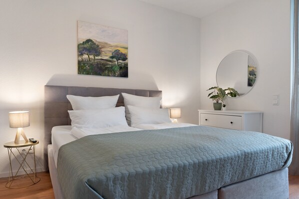 A bedroom with a bed, bedside lamps, a bedside table, a mirror, and a painting on the wall.