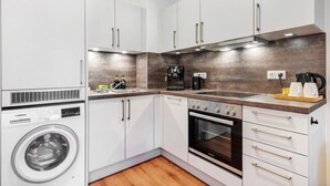 A modern kitchen with white cabinets, a built-in washing machine, a stove, and a coffee maker.