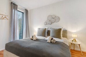 A bedroom with a large bed, a bedside table with a lamp, a wall decoration, and a window with curtains. - Apartment 'Km Style Apartments 7' with Balcony and Wi-Fi (Freiburg im Breisgau)