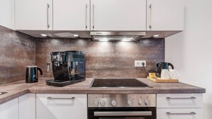 A modern kitchen with white cabinets, a built-in stove, an oven, and a coffee maker.